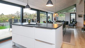 A modern kitchen with a large island, black pendant lights, and a view of the outdoors through large windows. - 5 Star Holiday Home in Hjorring (Hjørring)