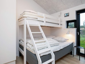 A bunk bed with a ladder, a bedside table, and a window with a view of greenery.