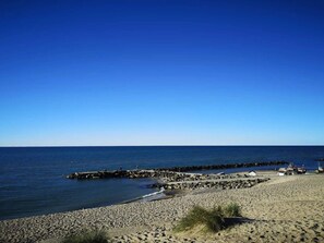 Een strand met een rotsenrijke zeewering, kalme zee en heldere lucht.