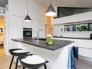 A modern kitchen with a central island, pendant lighting, and a view of the outside.
