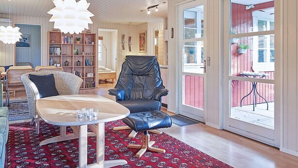 A spacious living room with a large window, a black leather chair, a wooden table, and a bookshelf. - 6 Person Holiday Home in Aakirkeby (Akirkeby)
