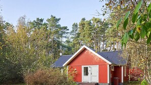 A red wooden cabin with a sloped roof, surrounded by trees and a grassy area. - 6 Person Holiday Home in Aakirkeby (Akirkeby)
