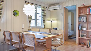 A cozy room with a wooden dining table, wicker chairs, a bookshelf, and a bed in the background. - 6 Person Holiday Home in Aakirkeby (Akirkeby)