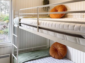 A bunk bed with two levels, a window with a view of greenery, and a radiator.