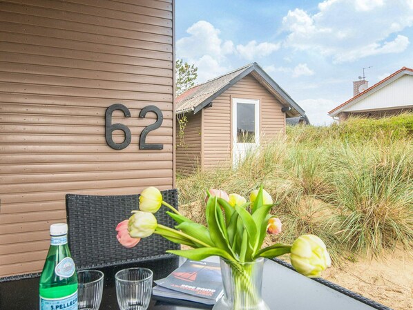 A table with a bottle, a glass, and a vase with flowers. A house number '62' is visible on the wall.