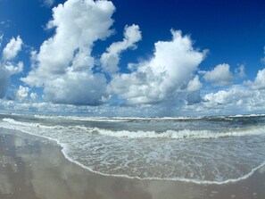 Une plage avec des vagues, du sable et un ciel partiellement nuageux.