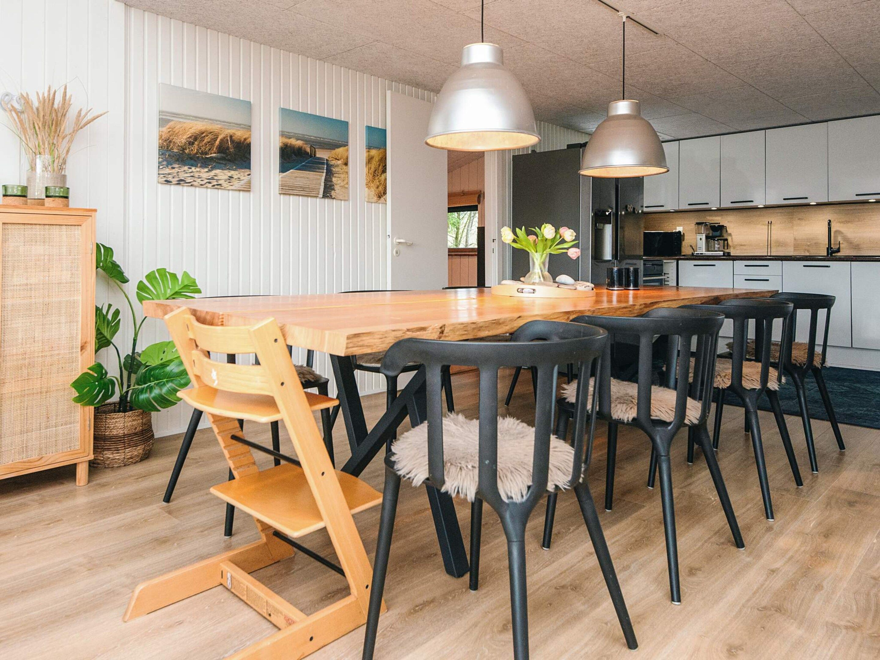Cozinha moderna com mesa e cadeiras de madeira, luminárias pendentes e vista para o exterior.