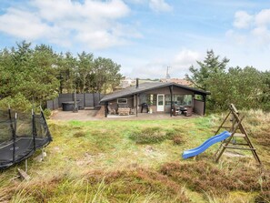 A house with a patio area, outdoor furniture, and a swing set. - 8 Person Holiday Home in Hvide Sande (Hvide Sande)