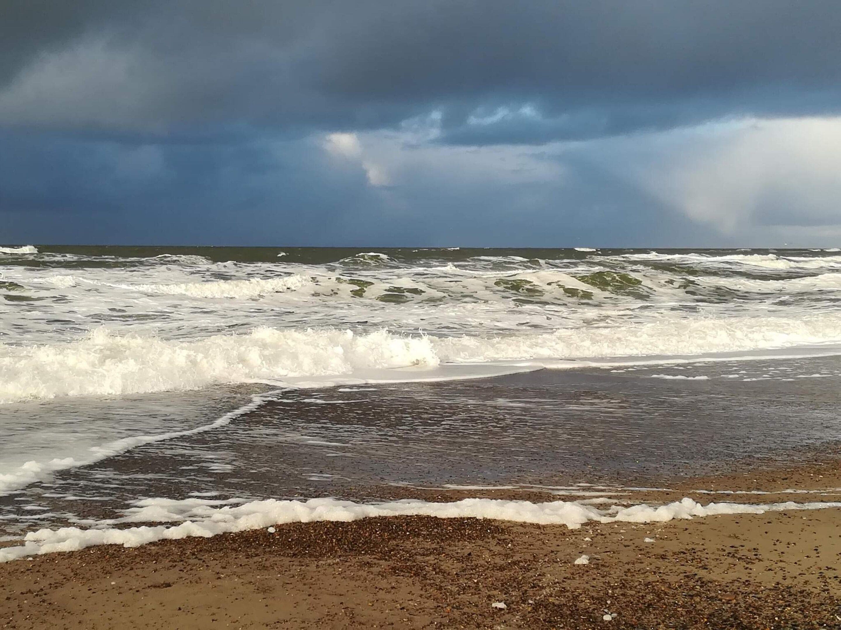 A beach with waves crashing onto the shore under a cloudy sky.