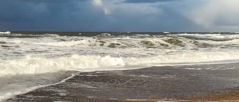 A beach with waves crashing onto the shore under a cloudy sky.