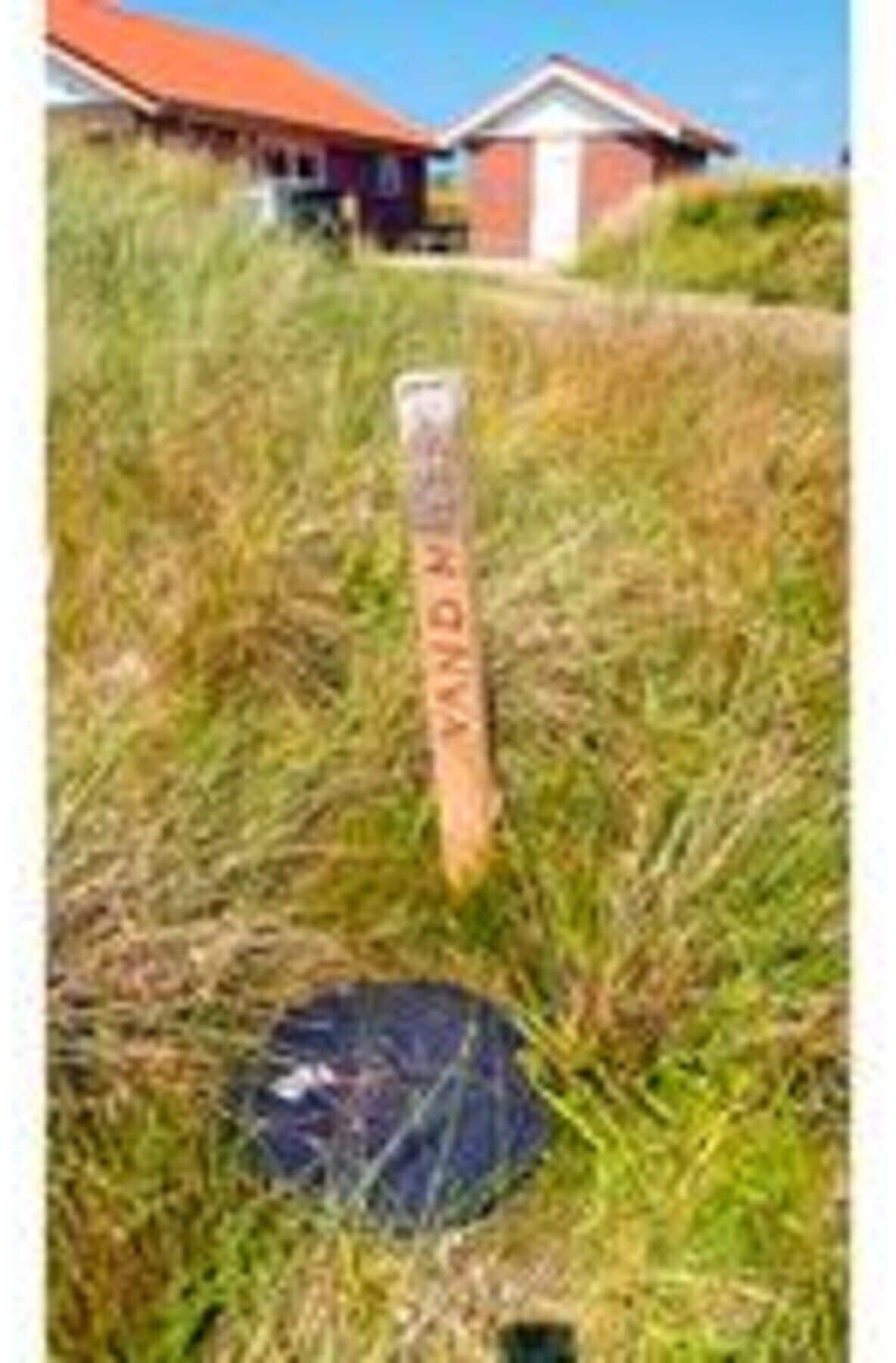 A wooden post with 'VANDER' written on it, standing in a grassy area with a red-roofed building in the background.