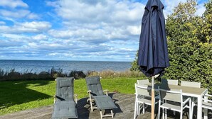 Une terrasse dotée de mobilier d’extérieur, comprenant des chaises longues et une table, et offrant une vue sur une étendue d’eau.