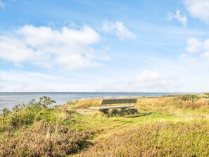 A bench by the sea with grassy terrain and a clear sky.