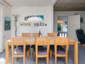 A dining area with a wooden table and chairs, a hanging light fixture, and framed pictures on the wall.