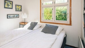 A double bed with white bedding, a window with a view of greenery, and framed pictures on the wall.