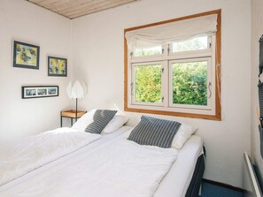 A double bed with white bedding, a window with a view of greenery, and framed pictures on the wall.