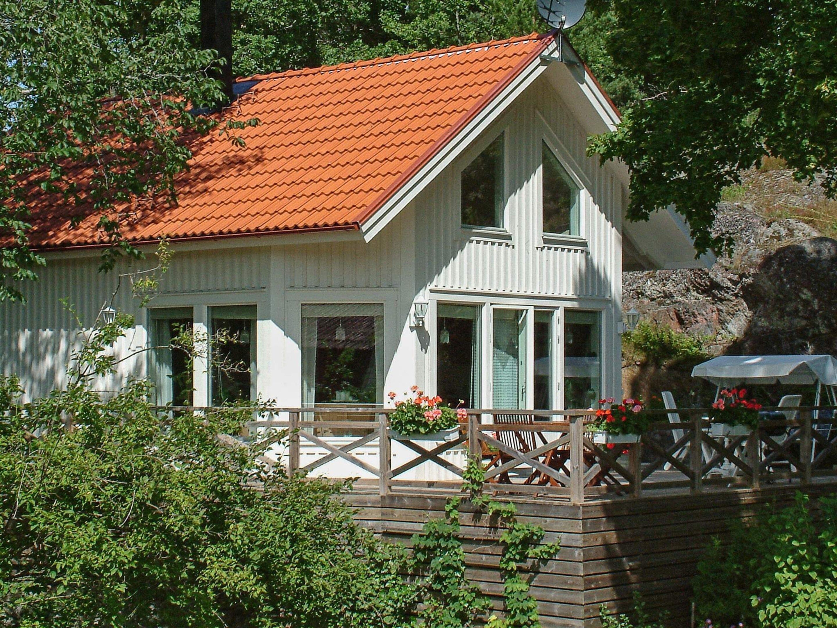 A white building with a red roof, a wooden deck, and a small outdoor seating area with chairs and a table.