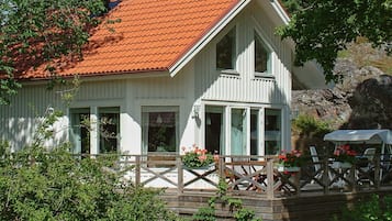 A white building with a red roof, a wooden deck, and a small outdoor seating area with chairs and a table.