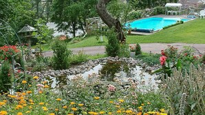 Ein Garten mit Teich, Schwimmbad und verschiedenen Pflanzen und Blumen.