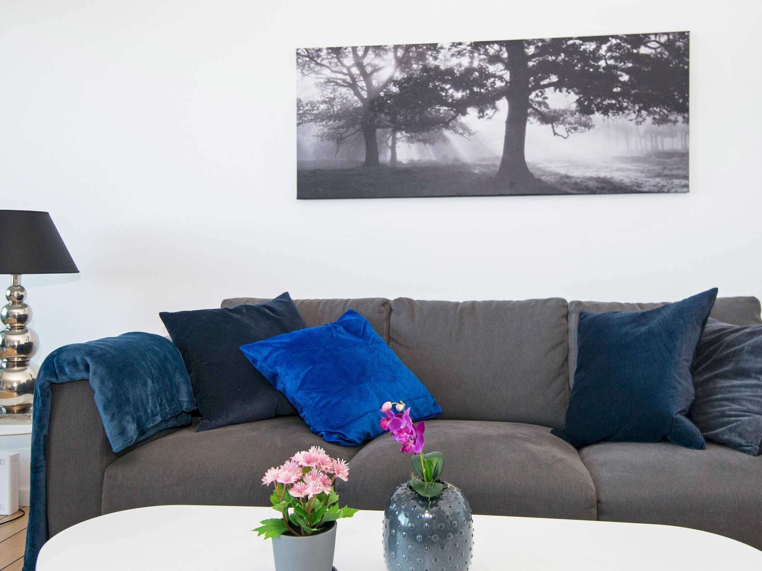A living room with a grey sofa, blue cushions, a white coffee table, and a framed picture on the wall.