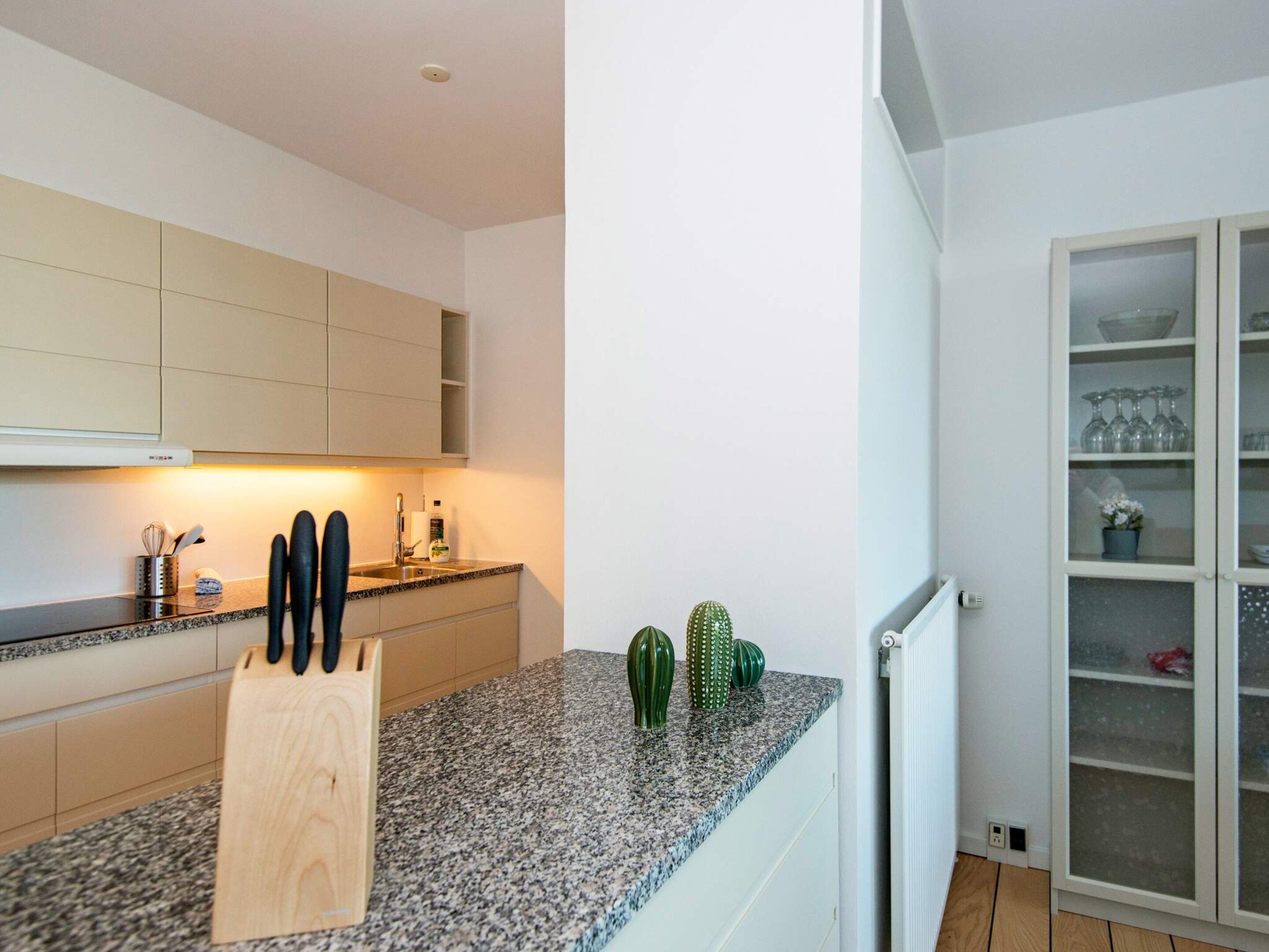 Eine Küche mit einer Granitabdeckung, einem Holzer Schneidebrett und einem Schrank mit Küchenutensilien.