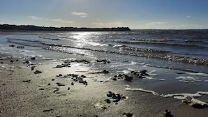 A beach with waves, a clear sky, and a distant landmass. - 5 Star Holiday Home in Ebeltoft (Ebeltoft)