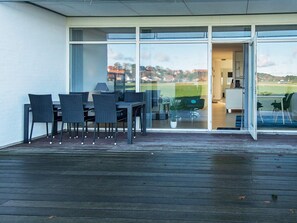 Une terrasse extérieure avec une table et des chaises, une porte vitrée donnant sur un espace intérieur, et une vue sur un quartier résidentiel.