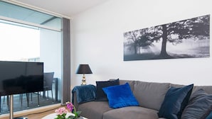 A modern living room with a grey sofa, a white coffee table, a TV, and a painting of trees. - 5 Star Holiday Home in Ebeltoft (Ebeltoft)