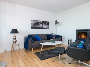 Un salon moderne avec un canapé gris, une table basse ronde, un fauteuil noir, une cheminée et un lampadaire.