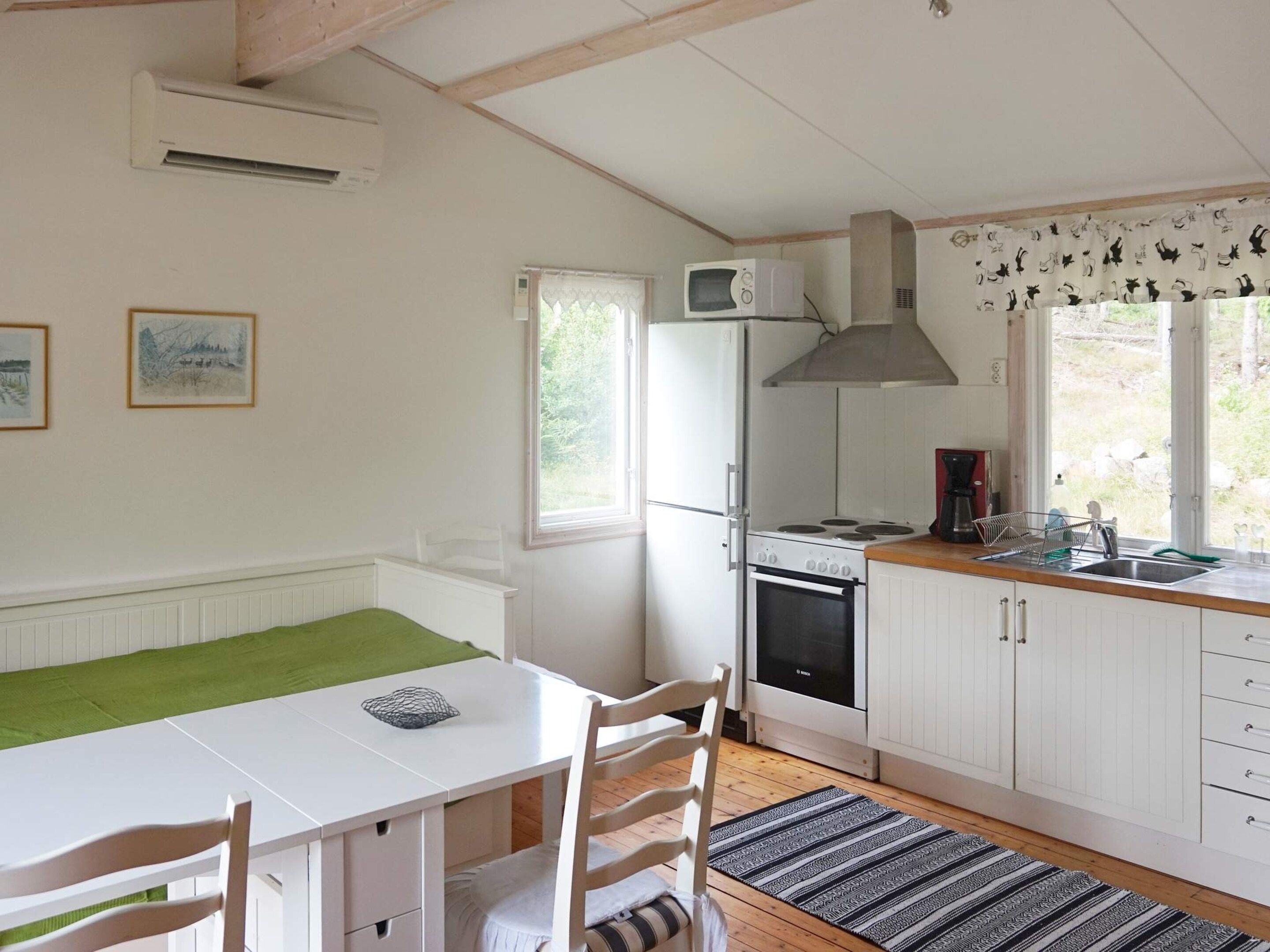 A compact kitchen with a refrigerator, stove, and microwave. There is a dining table with chairs and a window with curtains.