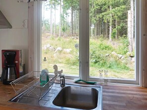 A kitchen with a stainless steel sink, a dish drying rack, a coffee maker, and a window with a view of a forest. - 4 Person Holiday Home in Smedstorp (Smedstorp)