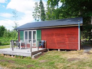 A small red wooden cabin with a porch and a table with chairs.