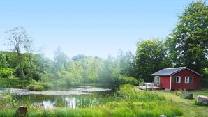 En hytte ved søen med en anløbsbro, omgivet af frodig vegetation og et roligt søområde.