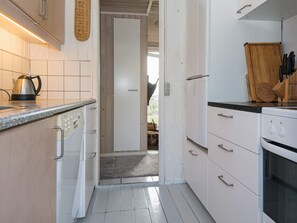 A kitchen with white cabinets, a countertop, a kettle, and a cutting board.