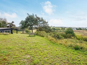 A grassy field with a picnic table and a small building with a sloped roof.