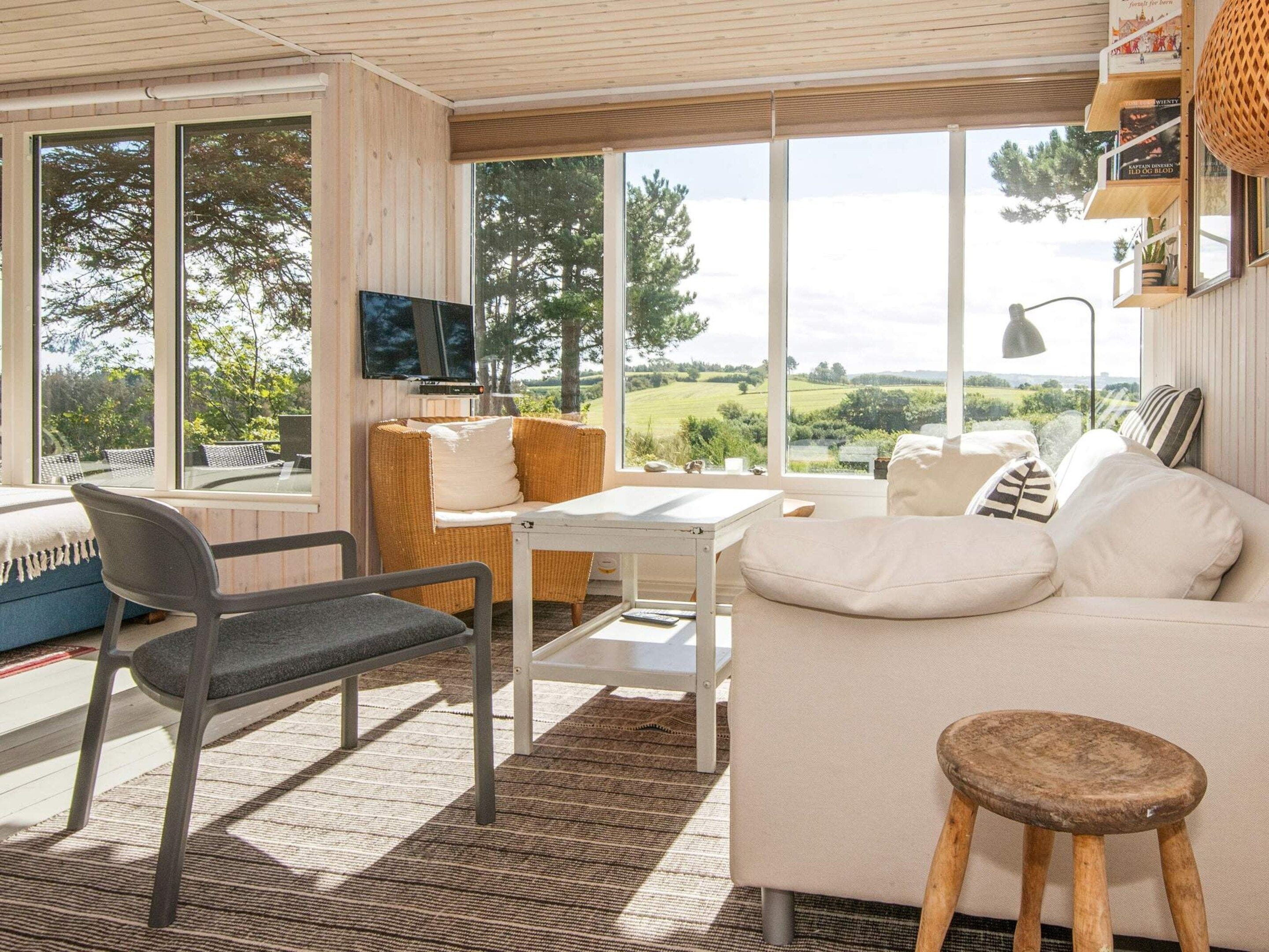 Un salón moderno con sofá, sillones, una mesa y televisión. Amplios ventanales ofrecen vistas al exterior.