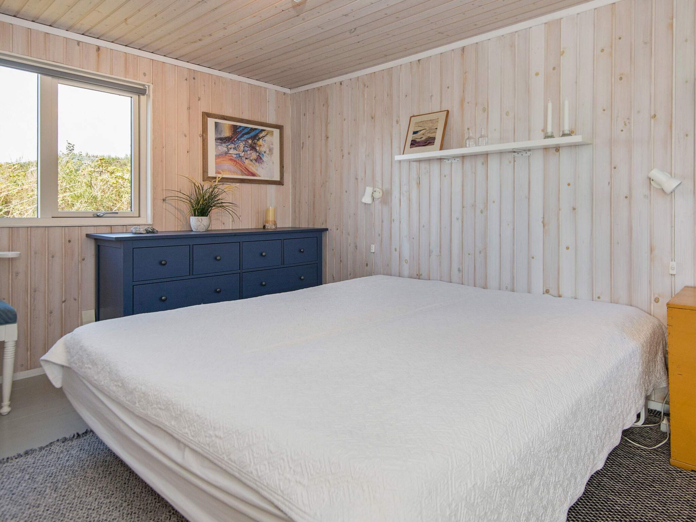 A bedroom with a large bed, a dresser, a window, and a wall-mounted shelf with decorative items.