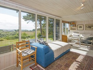A room with a large window, a blue sofa, a wooden chair, a small table, and a bookshelf. - 8 Person Holiday Home in Knebel (Knebel)