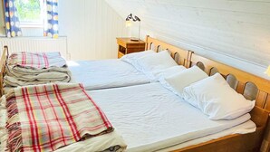 Ein Doppelbett mit Holz Kopfteil, ein Nachttisch mit Lampe und ein Fenster mit Vorhängen.