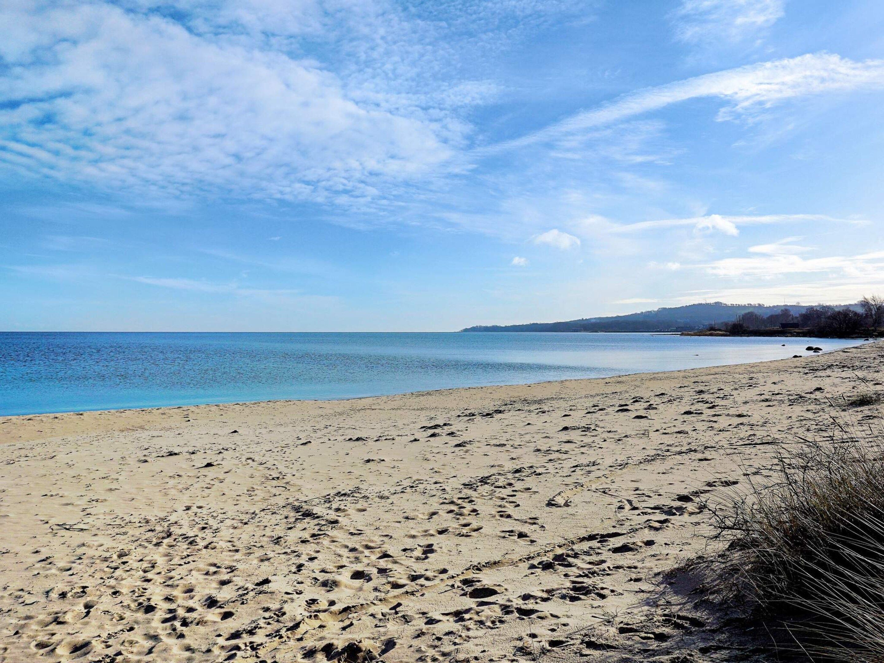 Une plage où l’on peut voir des empreintes de pas dans le sable, un ciel dégagé et une mer calme.