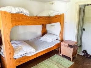 A bunk bed with a wooden frame, two pillows, a small bedside table, and a green rug.