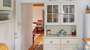 Eine Küche mit weißen Schränken, einem Holzbstuhl, einem Tisch mit floralem Tischläufer und einer Uhr an der Wand.