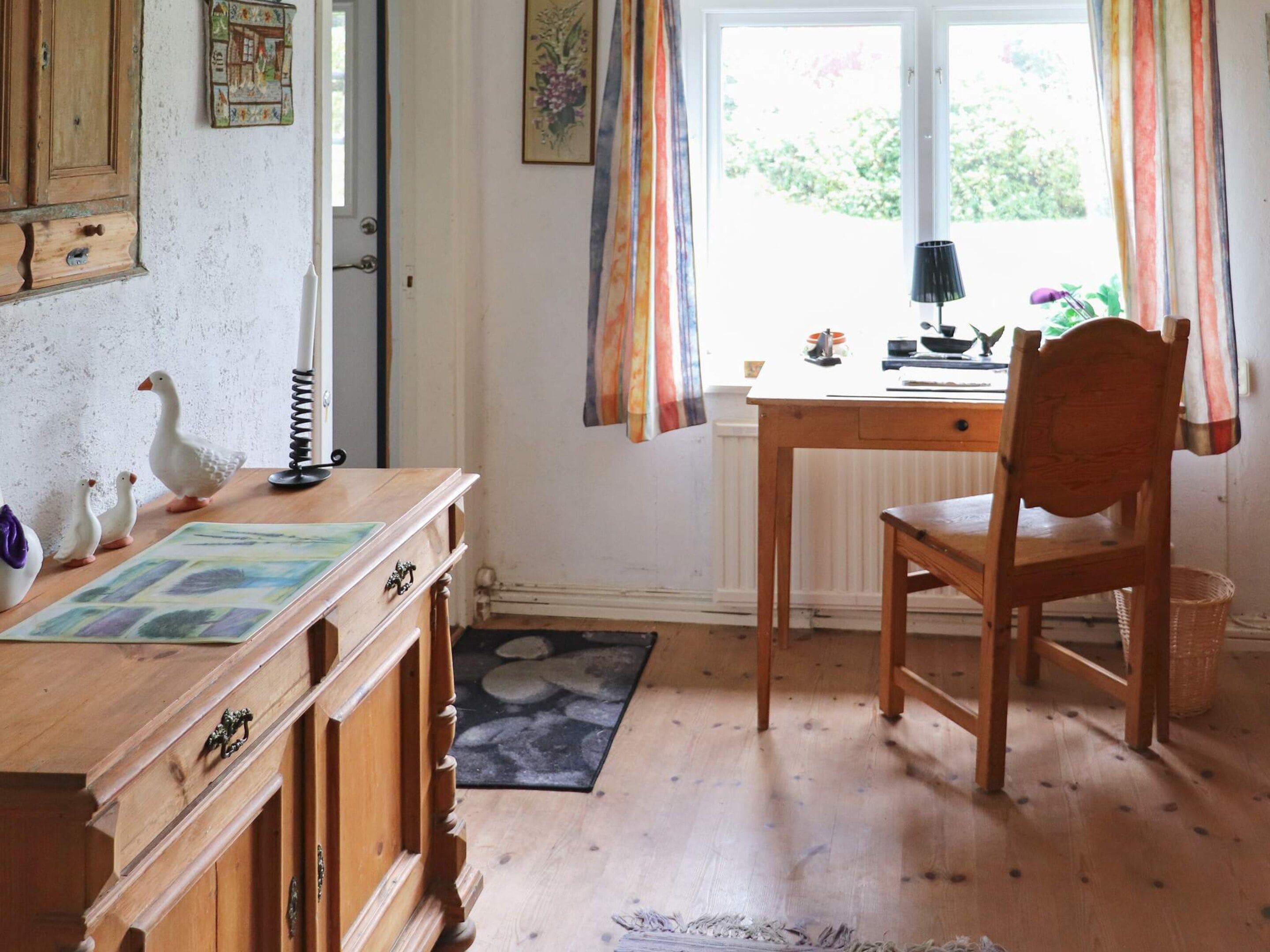 A room with a wooden desk, a chair, a radiator, a window with curtains, and a door.