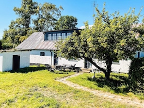 A rustic building with a sloped roof, a small attached structure, and a paved path leading to a seating area with outdoor furniture. - 10 Person Holiday Home in Hammenhog (Hammenhög)