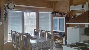 A wooden cabin interior with a dining table, chairs, a clock, and a kitchenette. - Holiday Home in Austbø (Alstahaug)