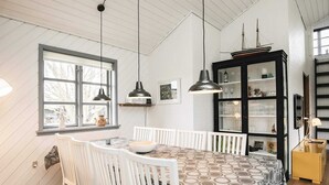 A dining area with a table and chairs, a window with curtains, pendant lights, and a black cabinet with glass doors. - 8 Person Holiday Home in Frorup (Frørup)
