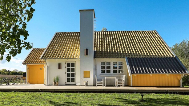 A two-story building with a tiled roof, a chimney, and a small porch with chairs. - 8 Person Holiday Home in Frorup (Frørup)