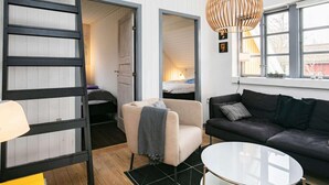A modern interior with a loft-style bed, a sofa, a chair, and a hanging light fixture. - 8 Person Holiday Home in Frorup (Frørup)