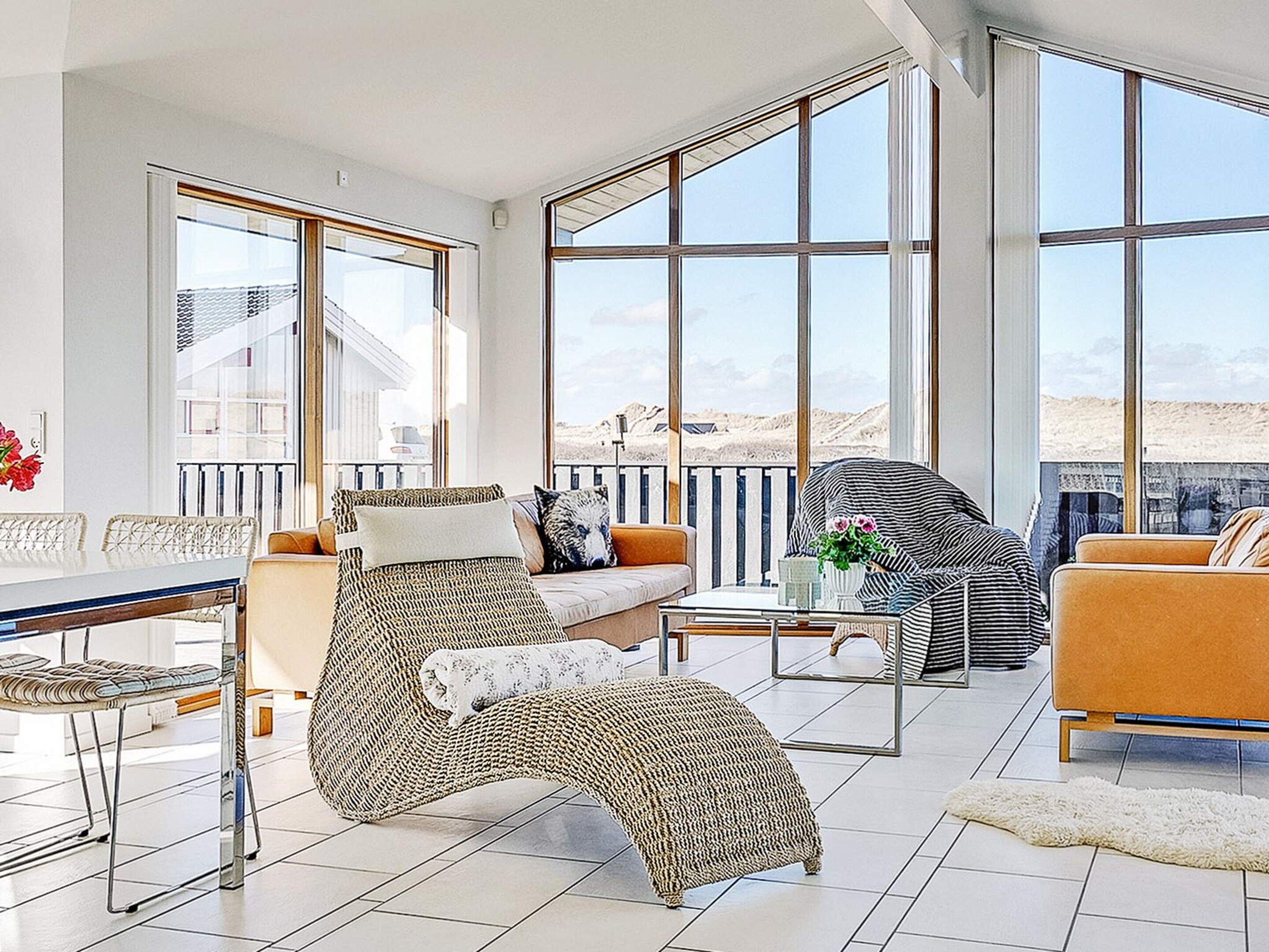 A spacious living area with a sofa, armchair, and coffee table, large windows offering a view of the outdoors.