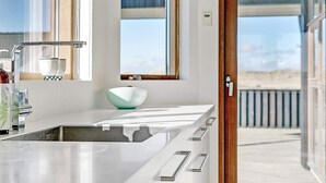 A modern kitchen with a large island, a window, and a view of the beach. - 5 Star Holiday Home in Hjorring (Hjørring)